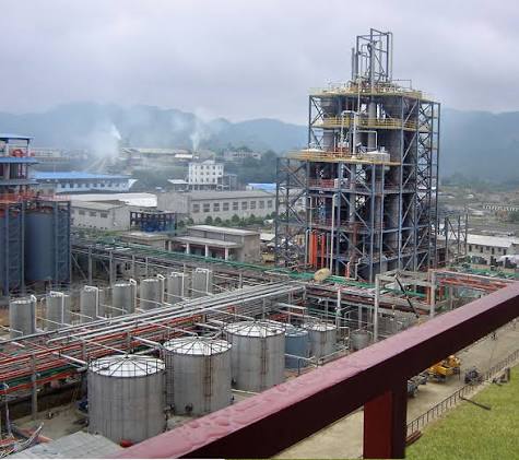 Outdoor industrial chemical plant with large cylindrical storage tanks, structural scaffolding, and processing towers for bulk phosphoric acid manufacturing
