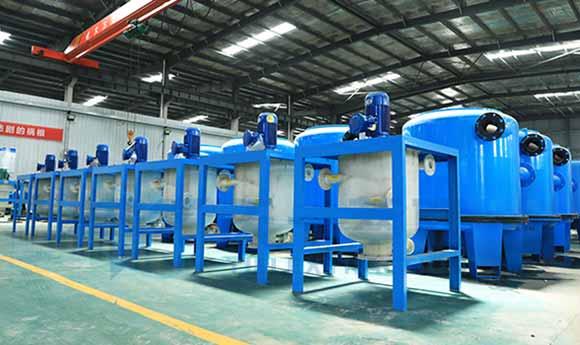 Row of industrial chemical filtration vessels and blue reaction tanks installed inside a chemical production facility