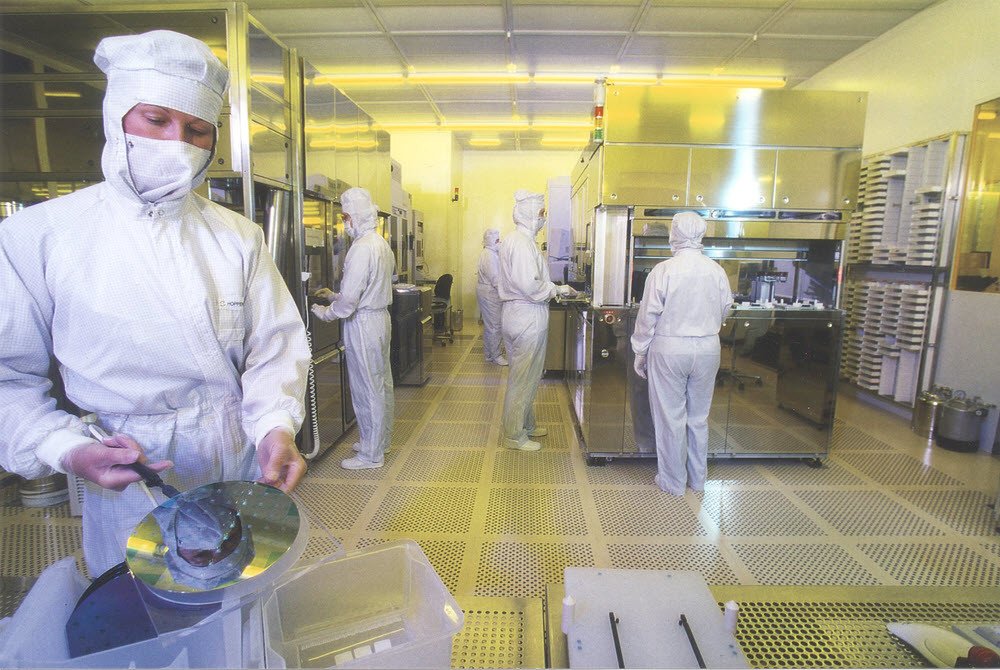 Technicians in cleanroom suits handling silicon wafers during semiconductor manufacturing