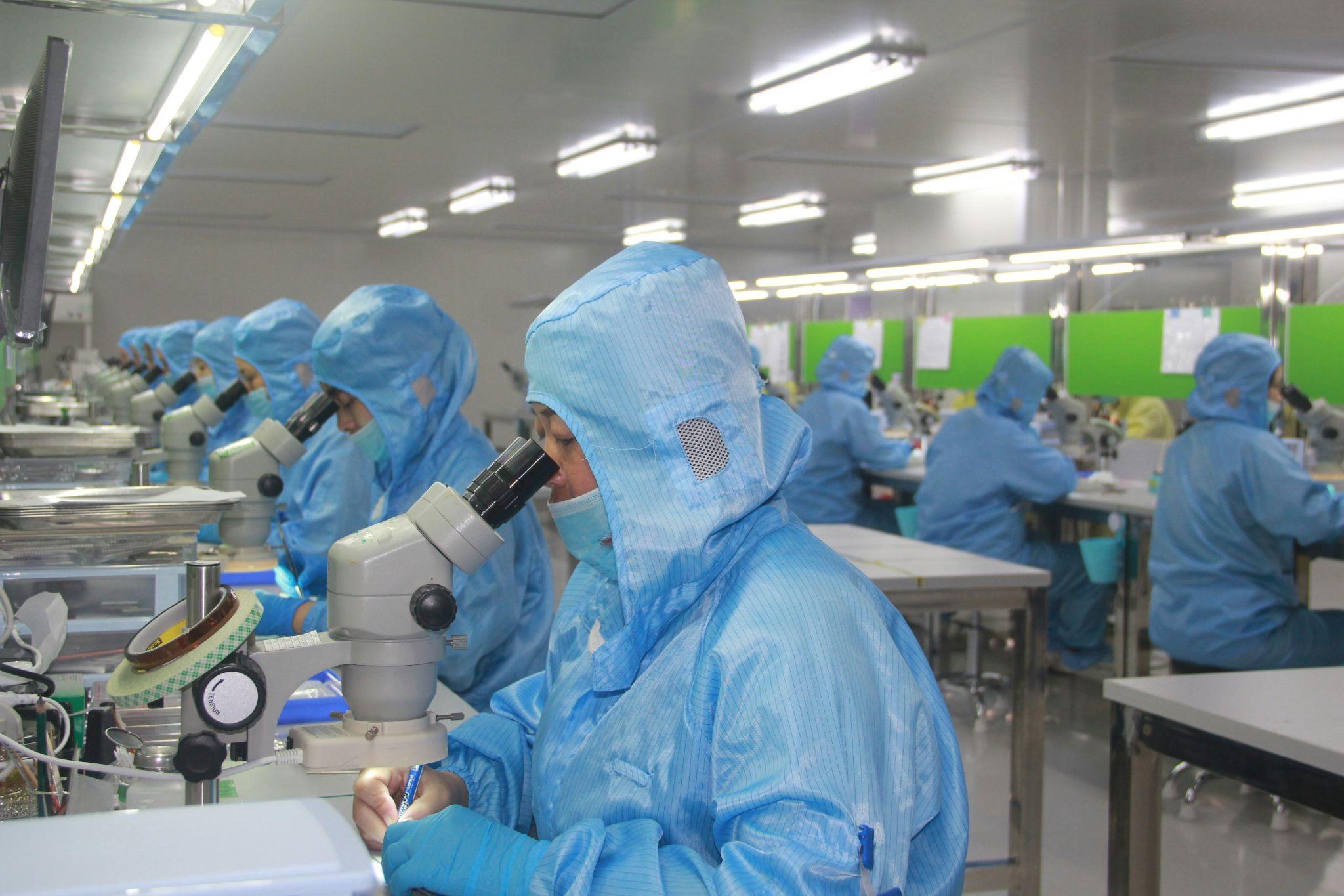 Technicians in full cleanroom suits using microscopes for high-precision quality inspection of semiconductor components and electronic materials