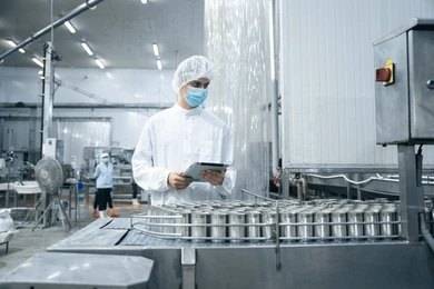 Phosphoric Acid in Food Industry and Food Additives 1 A bottle of food-grade phosphoric acid (E338) in a food processing facility with a faceless worker in the background.