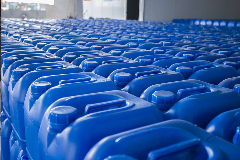 A row of blue plastic jugs of technical grade phosphoric acid 85% in a bright industrial warehouse.
