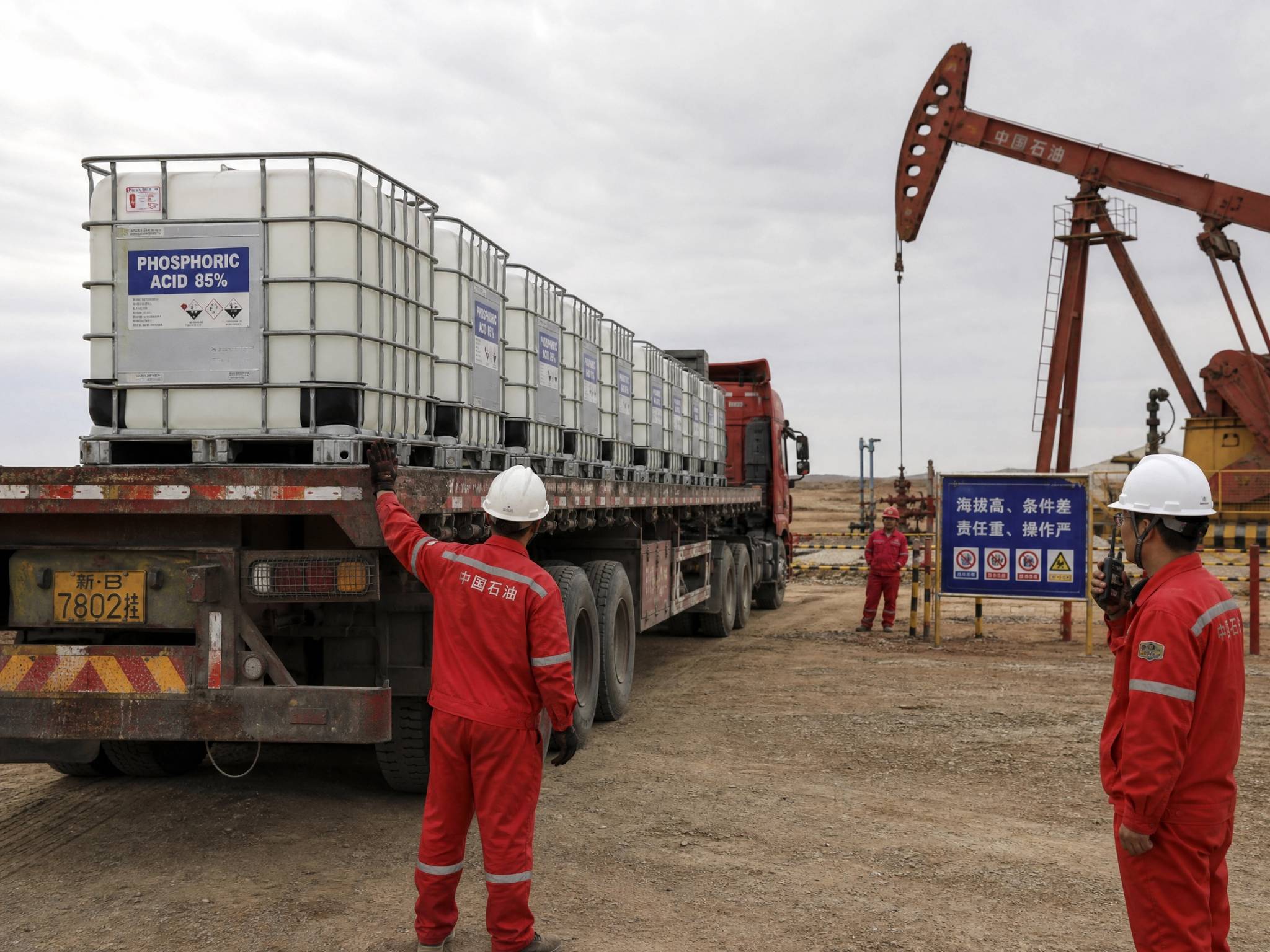 Workers loading phosphoric acid IBC tanks onto truck at oilfield site