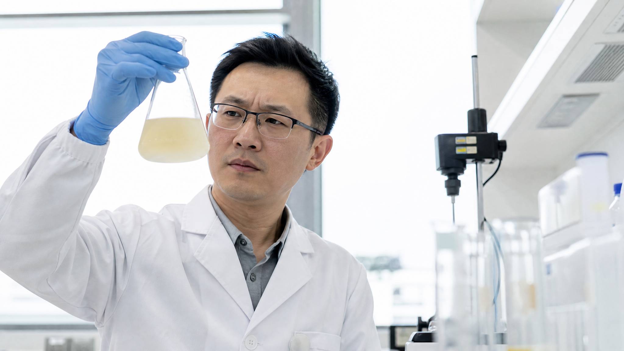 A professional Asian Chinese quality control manager in a modern laboratory. They are holding a clear glass flask containing a slightly yellowish, cloudy liquid, comparing it against a bright white background. They have a concerned expression. Professional, high-tech, photorealistic.