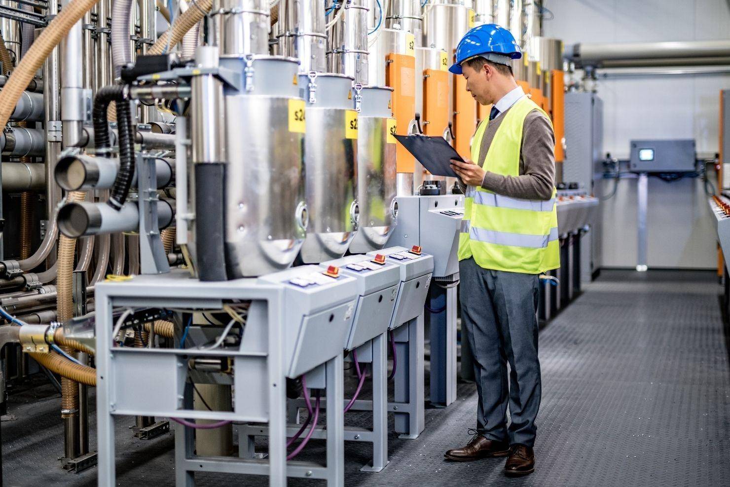 A faceless auditor in professional attire inspecting a chemical production line in China. They are holding a digital tablet and checking compliance labels on stainless steel equipment. Bright industrial lighting, clean environment, photorealistic.