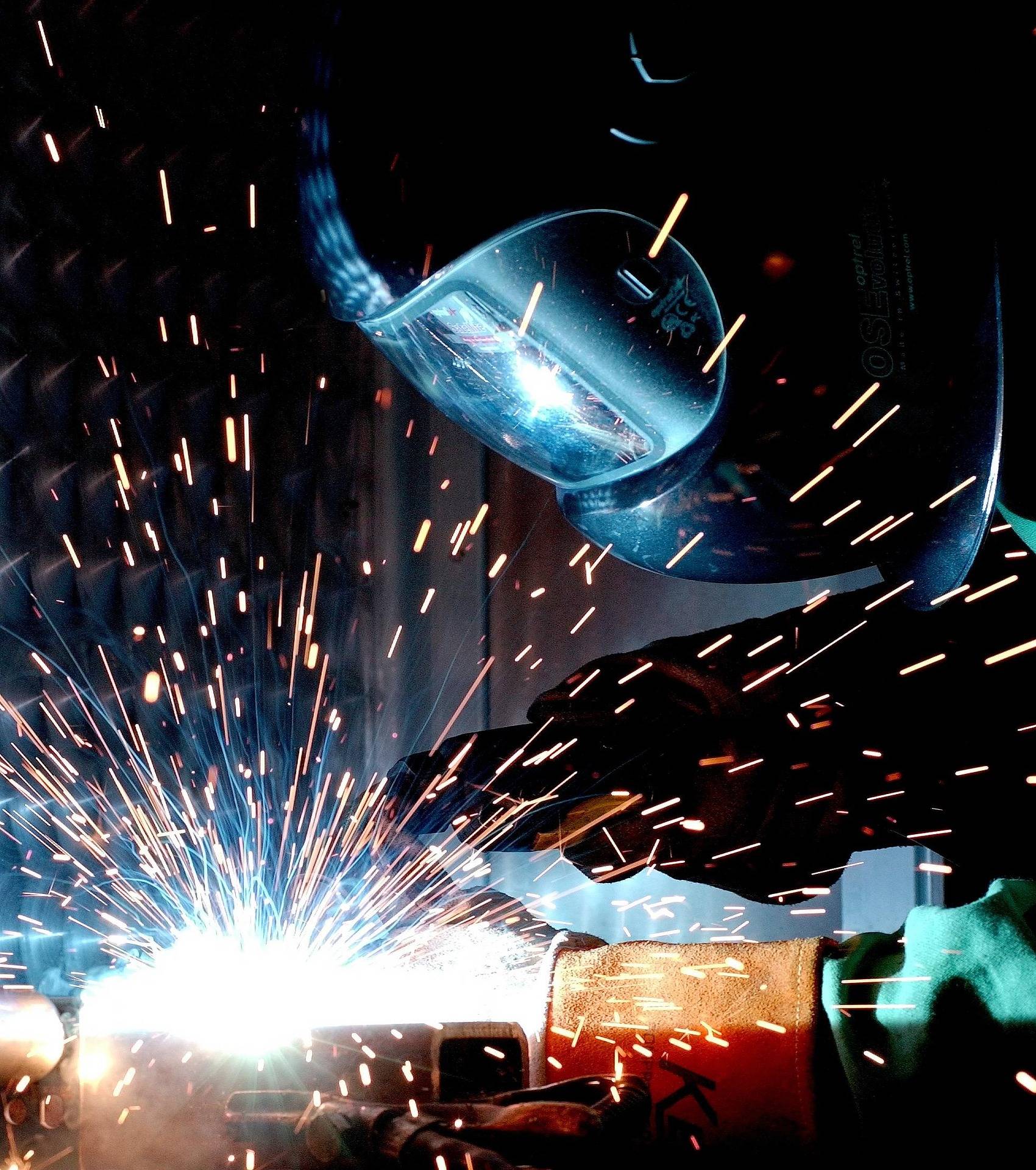Phosphoric Acid vs Oxalic Acid 2 A welder wearing a protective visor works on metal, producing a bright spray of sparks in an industrial setting.