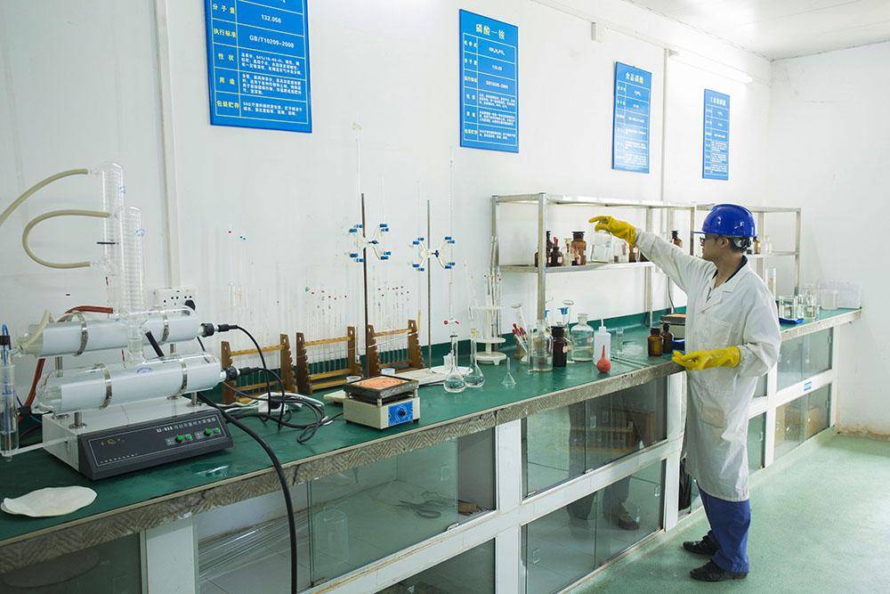 Phosphoric Acid vs Oxalic Acid 7 A lab technician in a white coat, yellow gloves, and blue hard hat reaches for chemical bottles in an industrial laboratory.