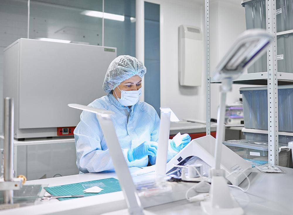 Laboratory technician performing quality control inspection in a sterile semiconductor or electronic-grade chemical testing facility