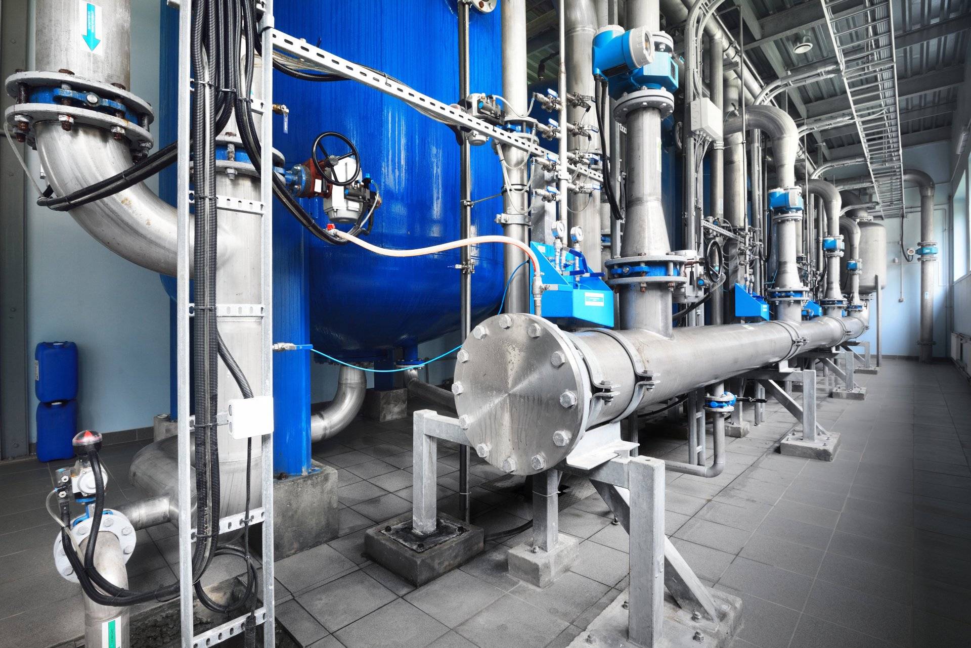 Industrial water treatment facility featuring blue storage tanks, stainless steel piping, and filtration equipment