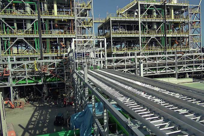 Outdoor view of a large chemical processing plant with steel scaffolding, green piping, and elevated pipe racks