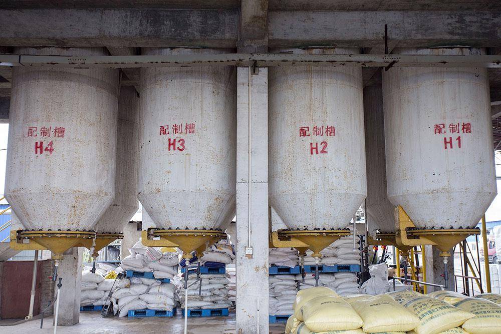 Row of large chemical blending tanks labeled H1 through H4 above stacked bags of raw materials at a phosphoric acid production facility